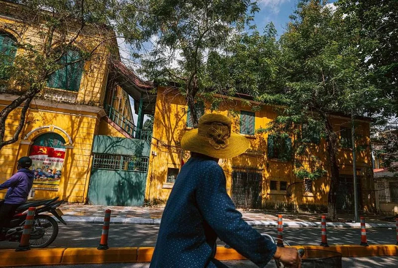 Travel From Hanoi To Haiphong Local Traffic Tips 5 A rider in a conical hat passing an old yellow colonial building on a quiet Haiphong street