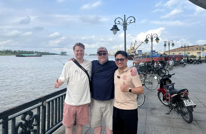 Guide and two travelers on the Cam River promenade near Hoang Van Thu Bridge in Haiphong