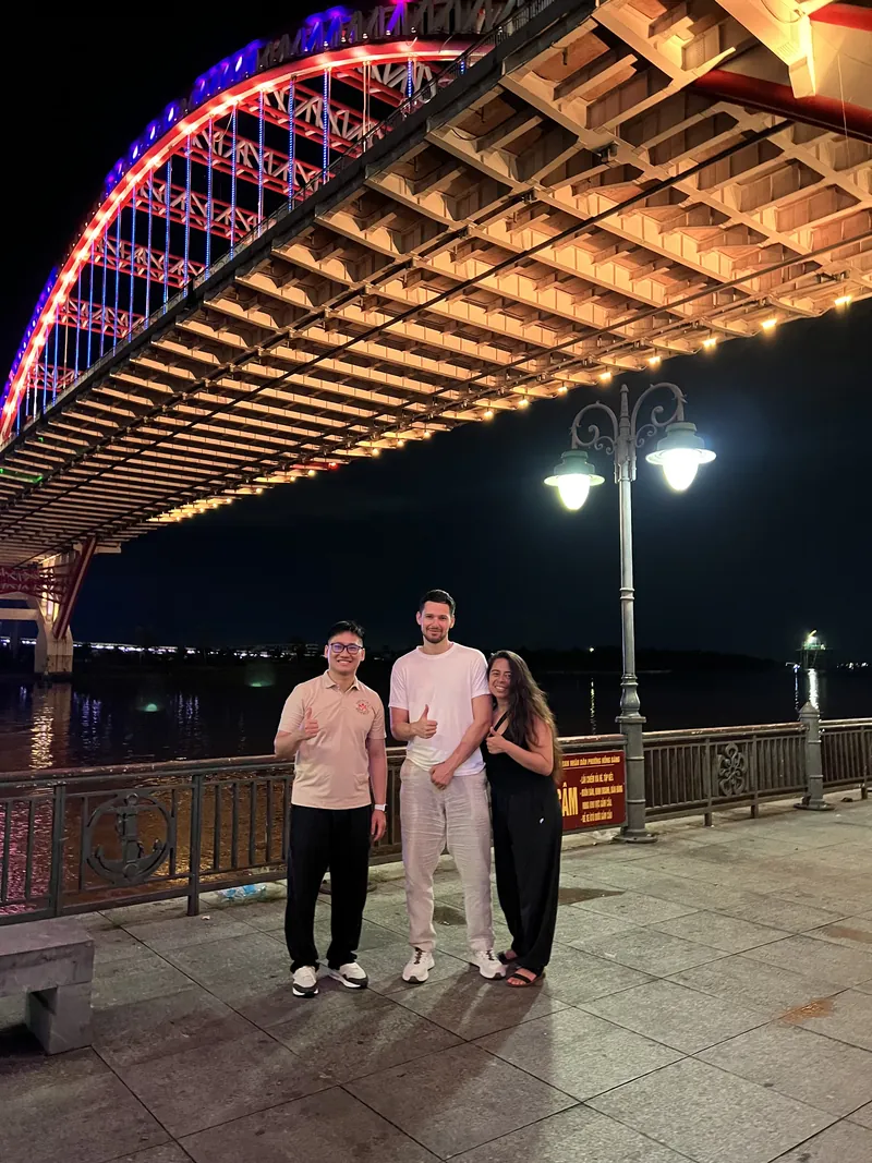 Guide and couple under the illuminated Hoang Van Thu Bridge in Haiphong at night