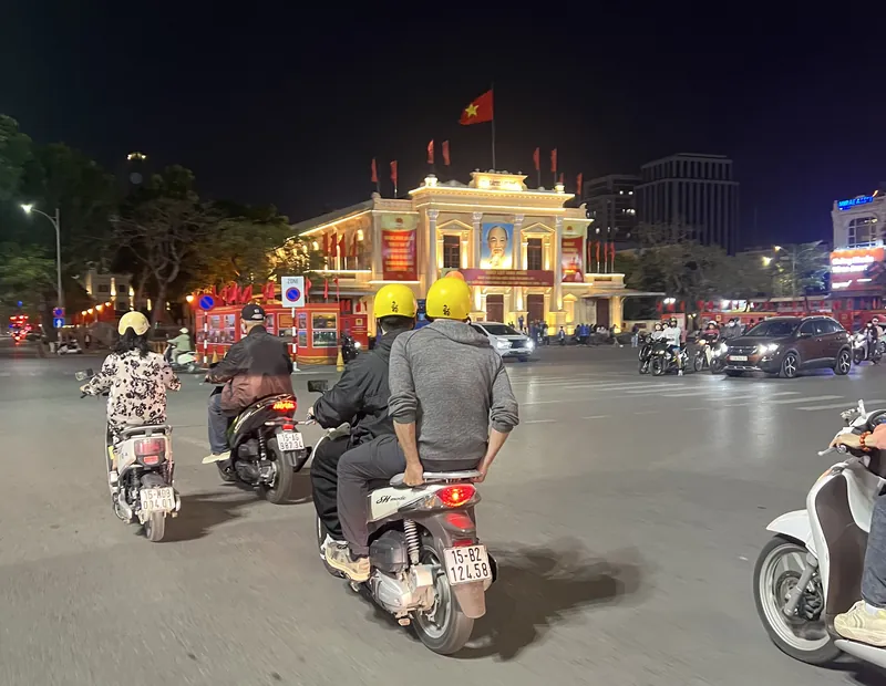 Riders on motorbikes passing Haiphong Opera House at night