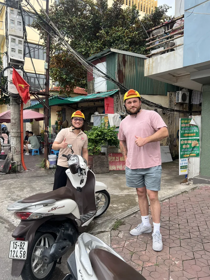 Tour guide in a duck helmet and a traveler stopping by a motorbike on a Haiphong street