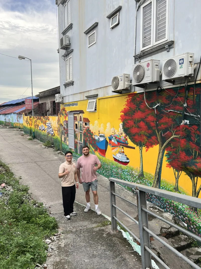 Guide and traveler walking along the mural street at the foot of Cau Quay bridge in Haiphong