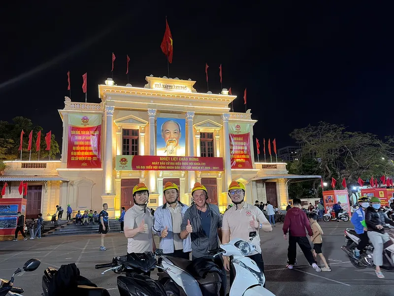 Motorbike tour group in yellow helmets in front of Haiphong Opera House at night