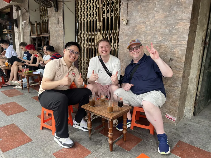 Guides and two travelers on plastic stools at a Haiphong sidewalk coffee shop